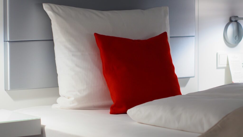 two white pillows and a red cushion on a bed